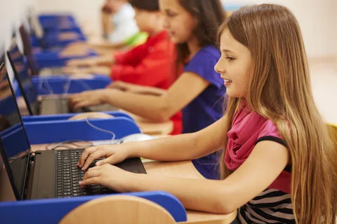 A group of children in pkg12 virtual academy focused on using computers in a bright classroom setting.